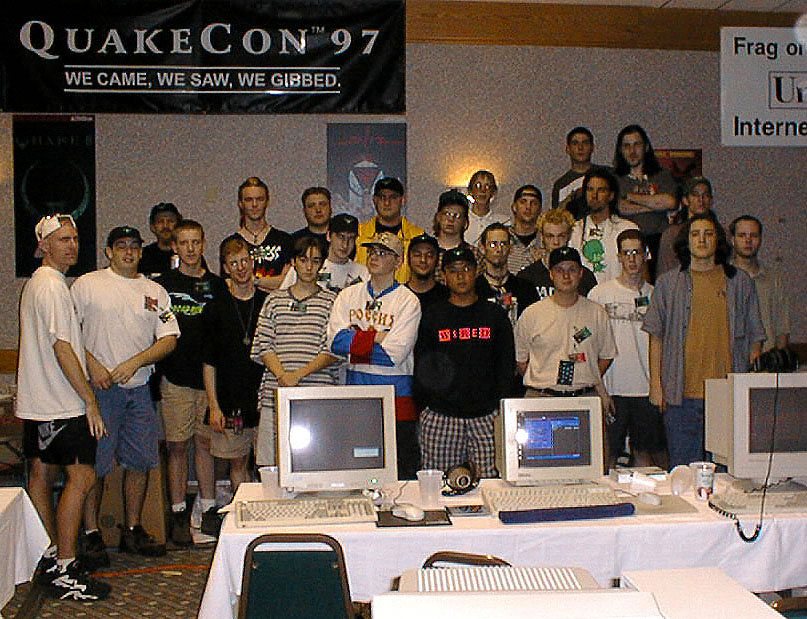 About thirty young people stand behind a row of beige CRT monitors under a banner reading QuakeCon 97, We came, we saw, we gibbed